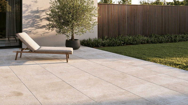 A modern patio of large light stone-look porcelain pavers with a lounge chair and potted olive tree