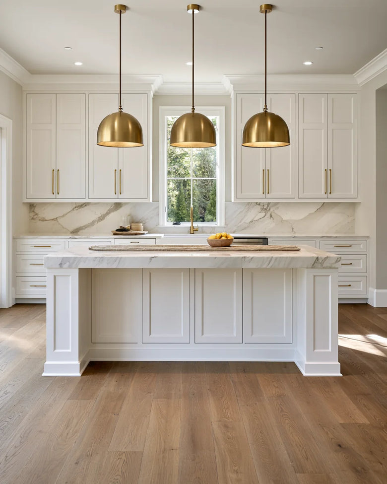 A white shaker kitchen with brass pendants, a marble island and wide oak floors
